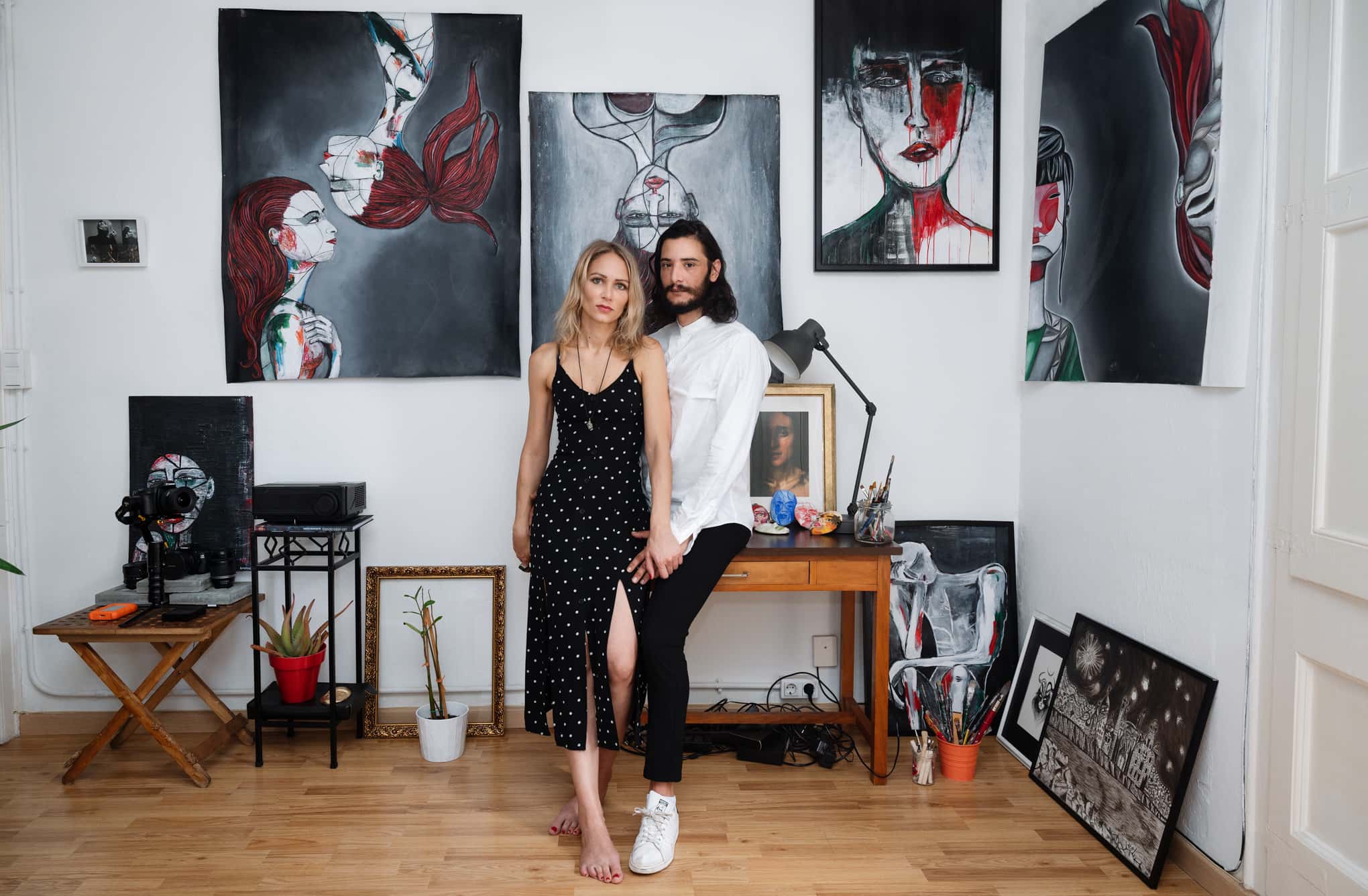 Anne Elizza y un compañero de pie en el estudio rodeados de sus cuadros