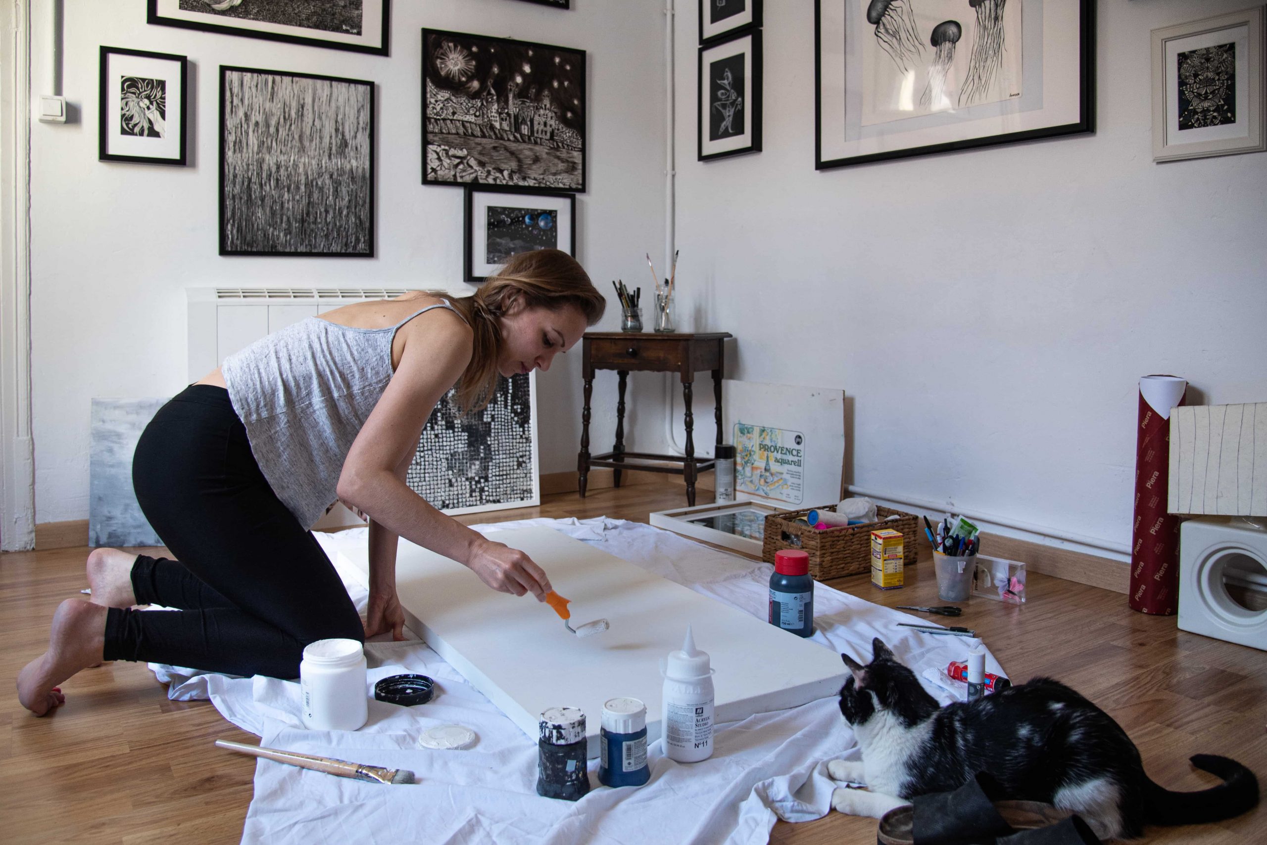 Anne Elizza pintando en el suelo de su estudio junto a un gato negro