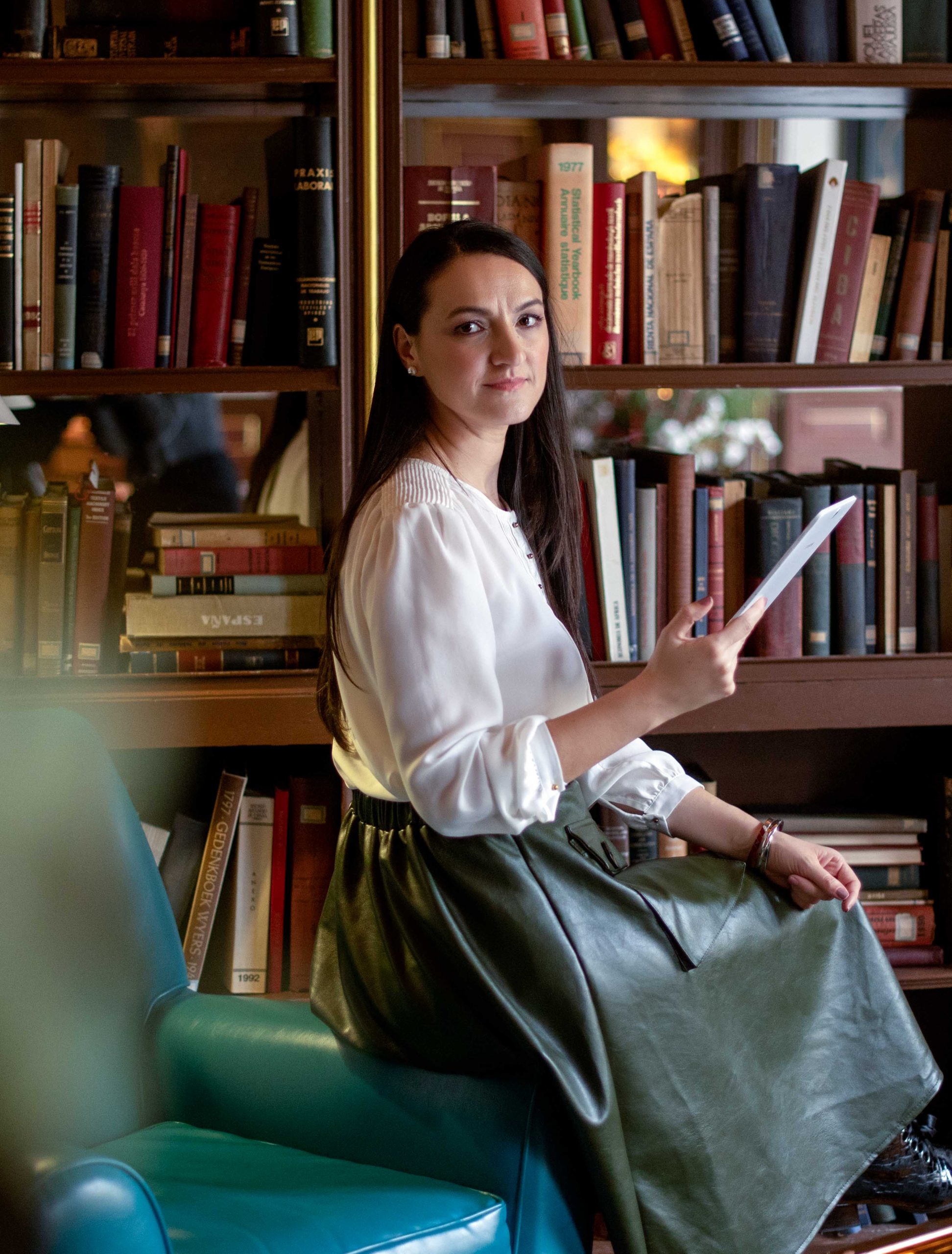 Daniela Constantin leyendo en un sillón delante de una biblioteca