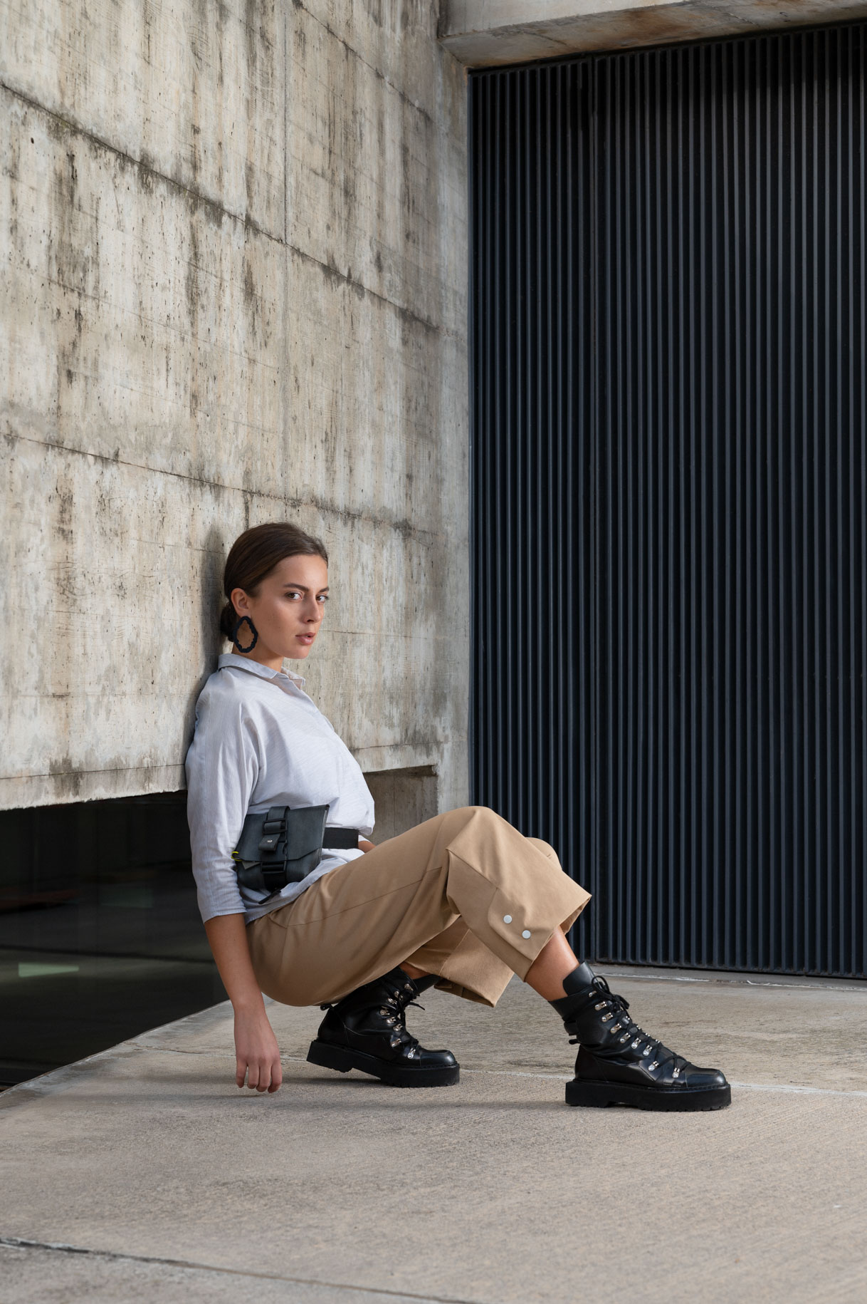 Modelo sentada en el suelo con pantalón camel y camisa gris