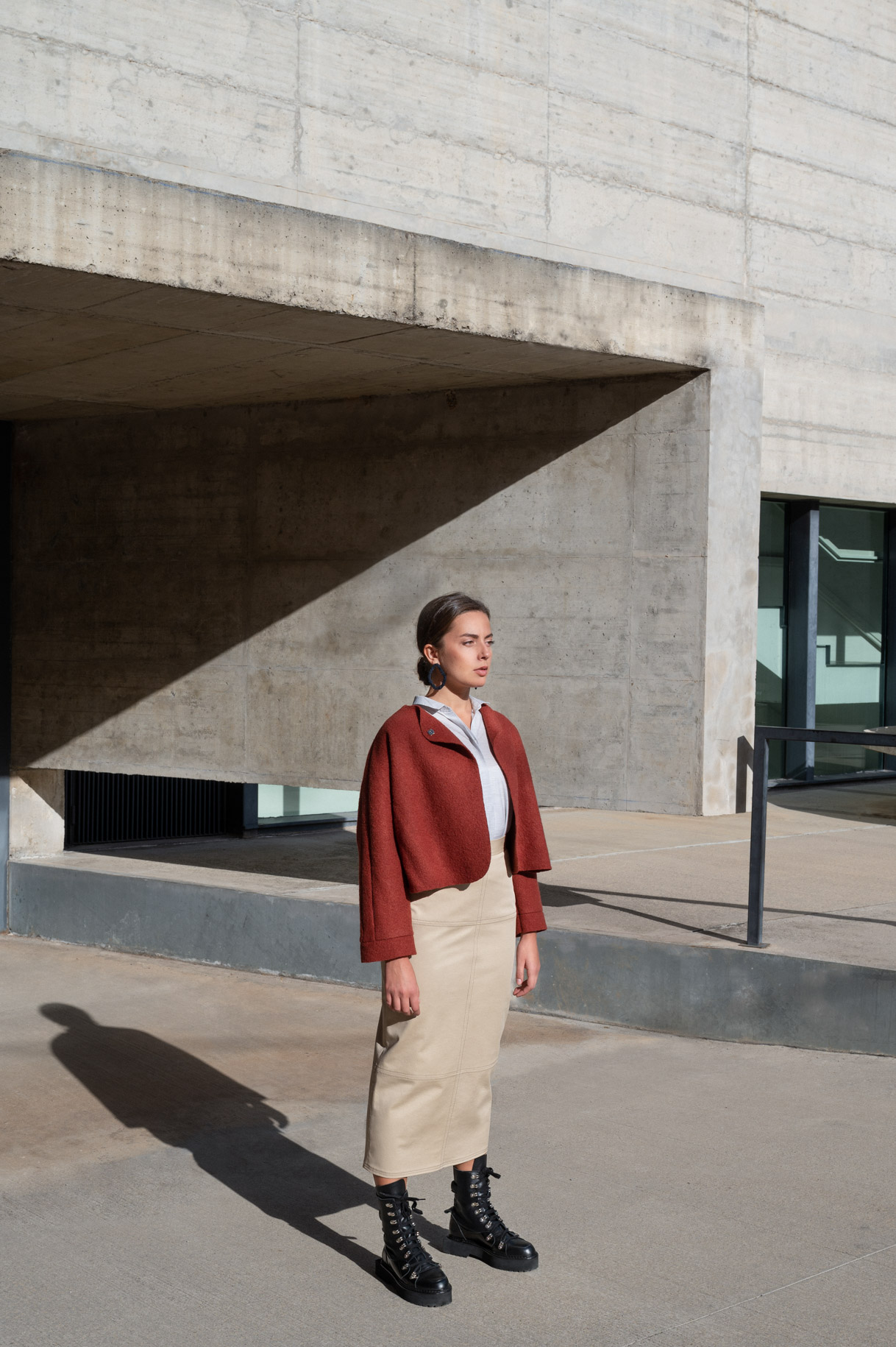 Modelo con chaqueta granate y falda beige ante un edificio de hormigón