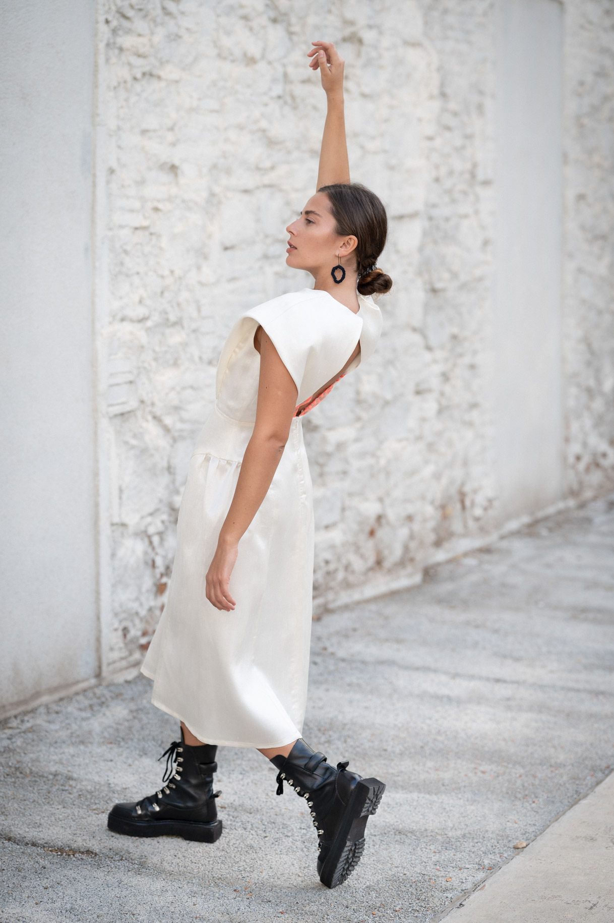 Modelo con vestido blanco y botas negras alzando el brazo