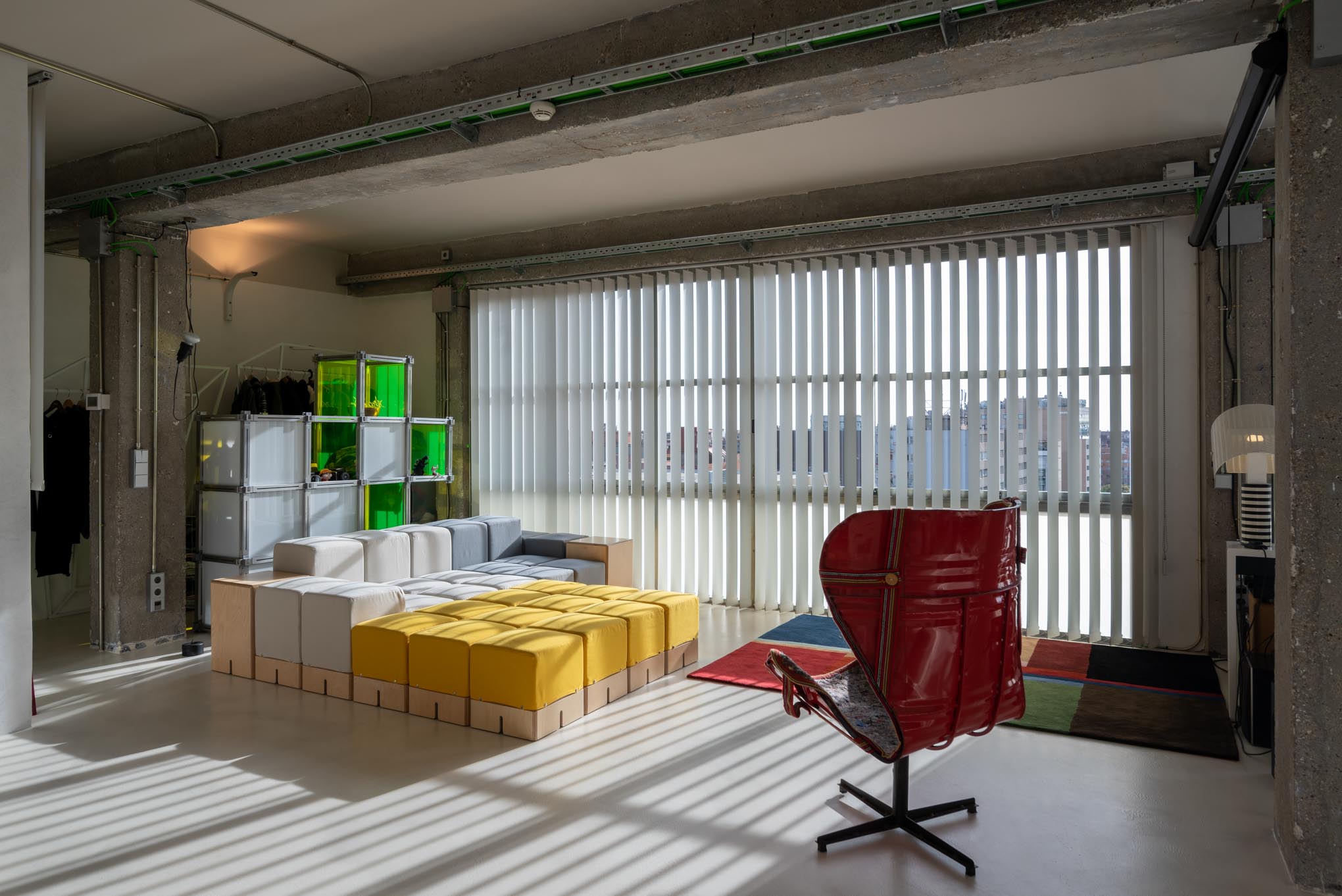 Sala de estar del loft industrial con estanterías modulares verdes y butaca roja