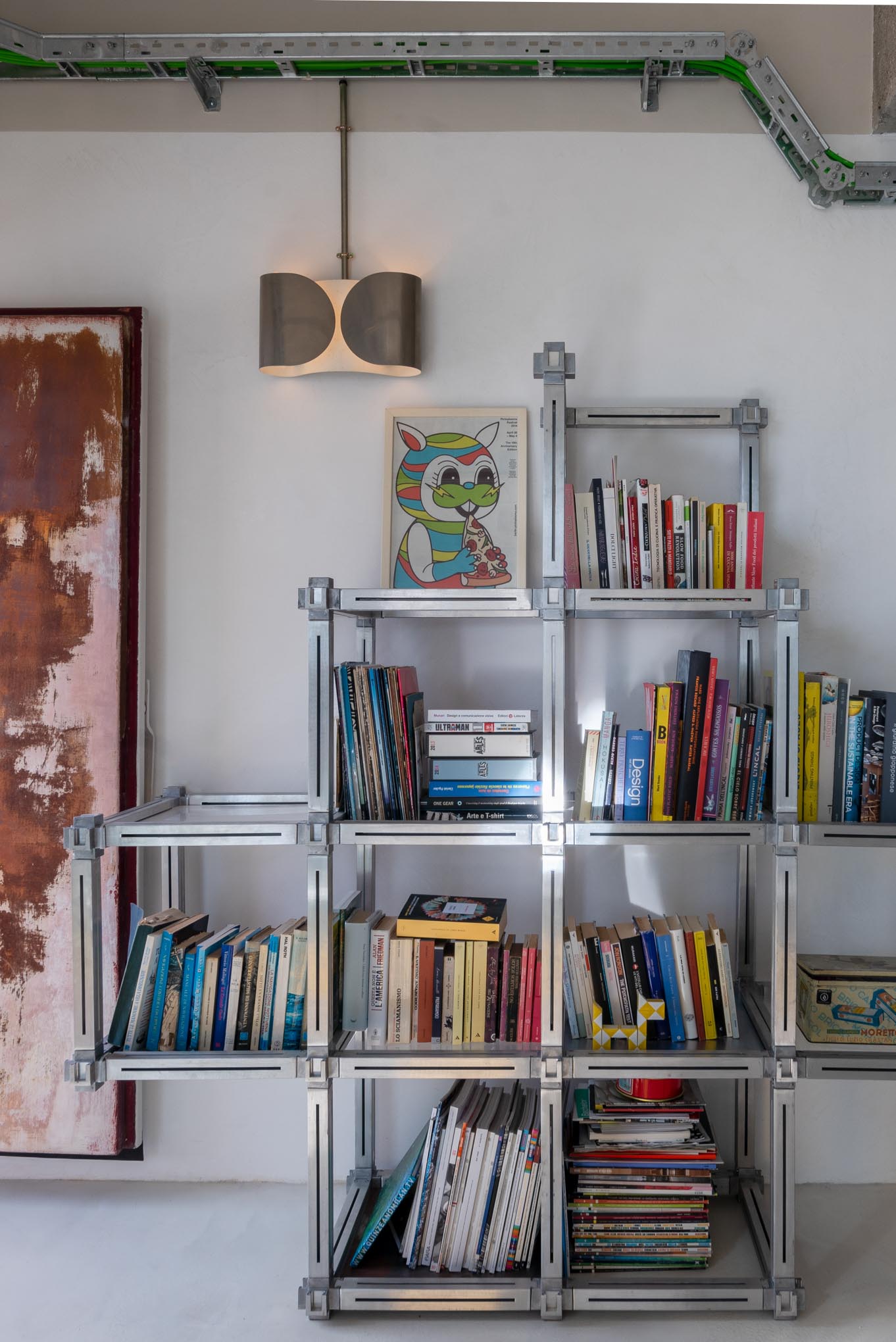 Estantería modular de aluminio llena de libros junto a un muro desgastado