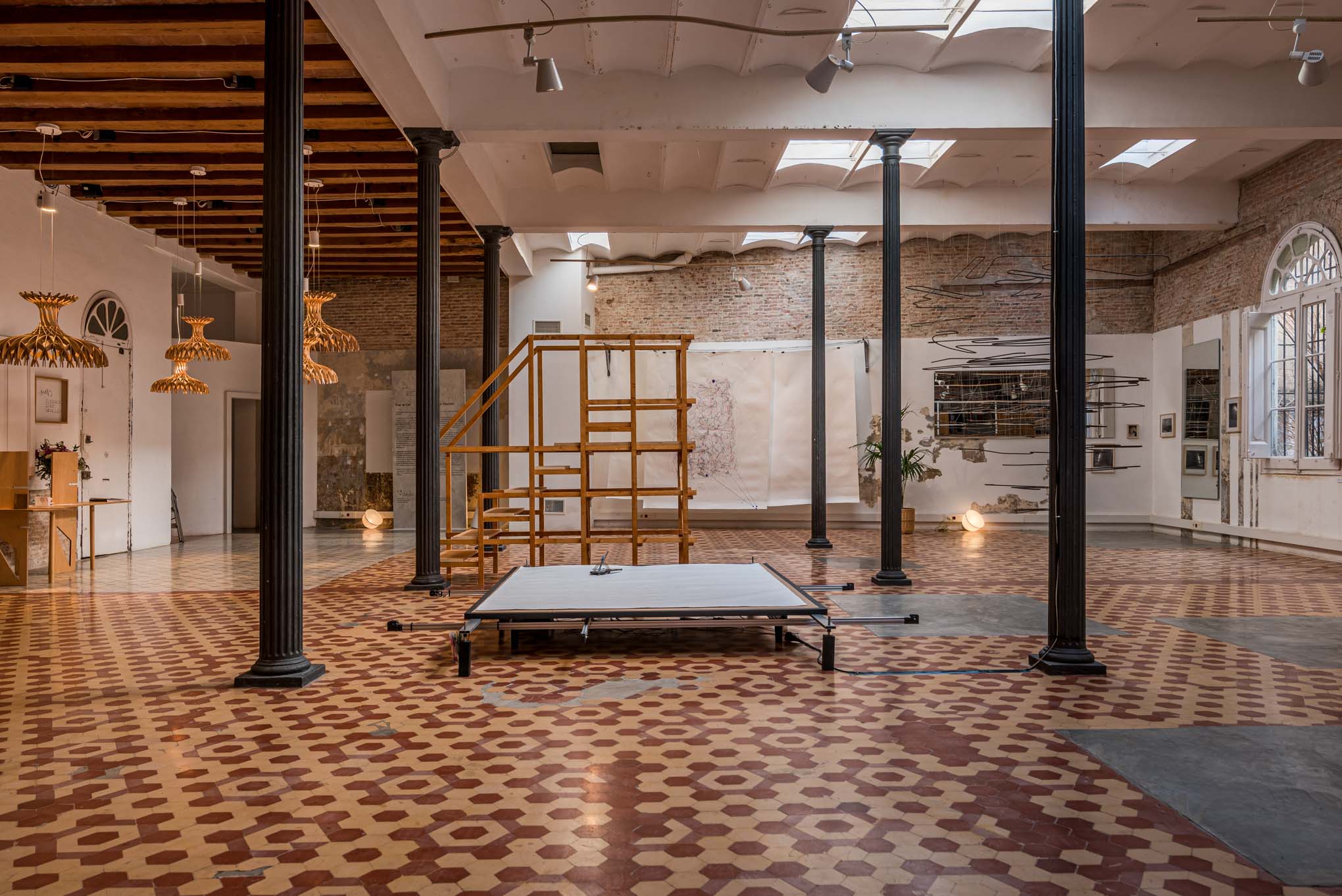 Vista de la sala de exposición con una plataforma de madera y obras colgadas en las paredes