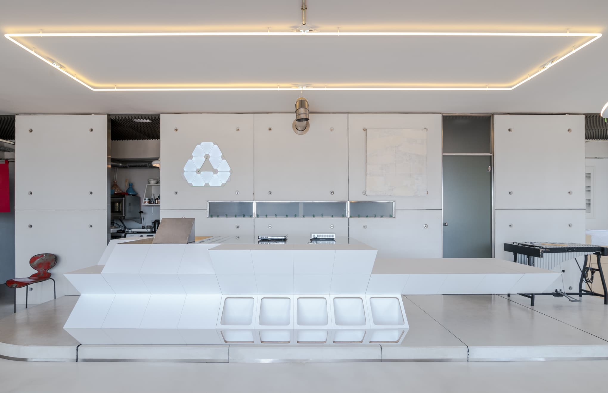 Espacio blanco monocromo con mobiliario geométrico y un marco de luz suspendido