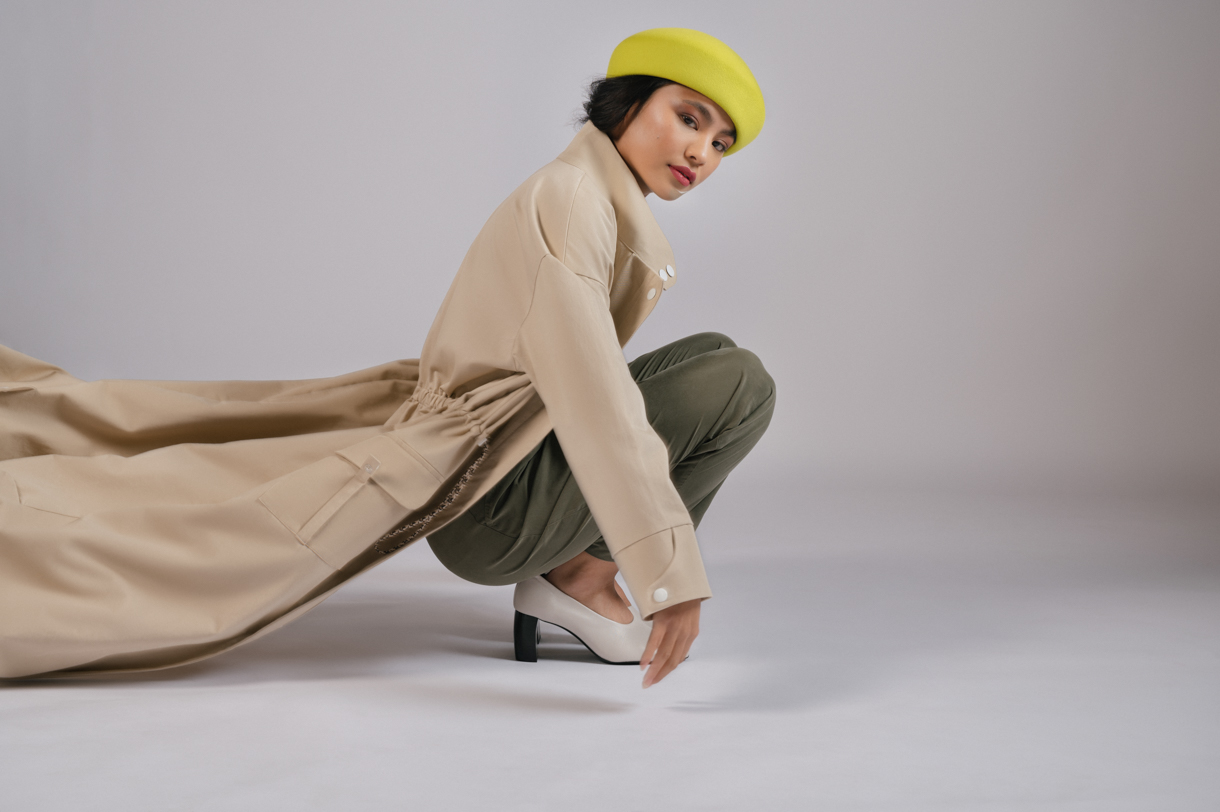 Modelo agachada con gabardina beige y gorro amarillo en estudio