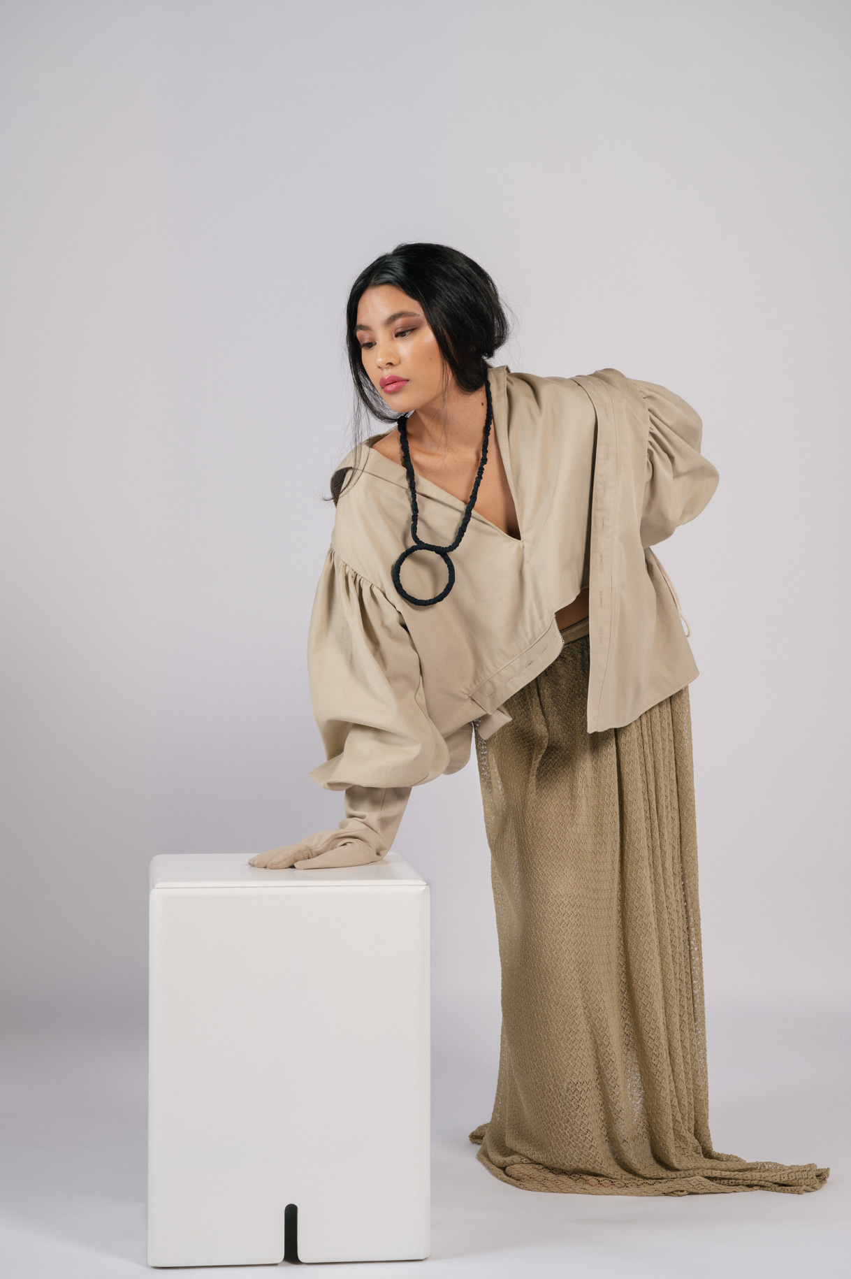 Modelo con conjunto beige y collar apoyada en un cubo blanco